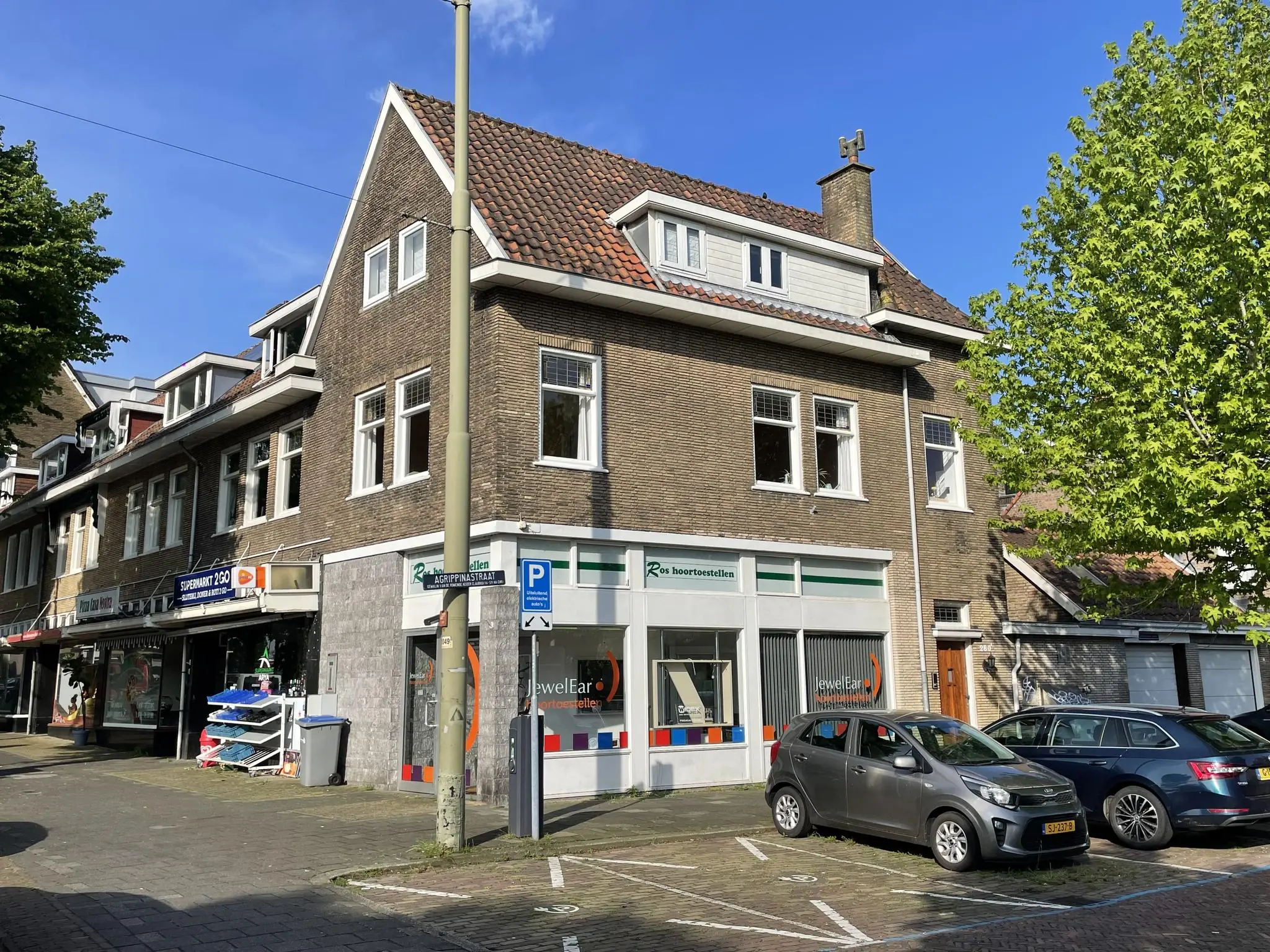 Hoekpand aan de Prinses Mariannelaan met winkels op de begane grond en geparkeerde auto's ervoor.